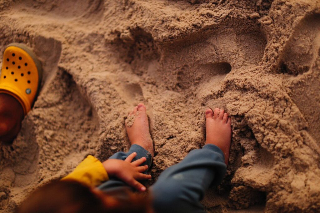 Child's feet and hands on sandy beach, capturing a playful moment in warm tones.