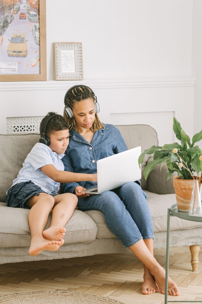 A mother and son sitting on a sofa, using a laptop with headphones, enjoying family bonding time.