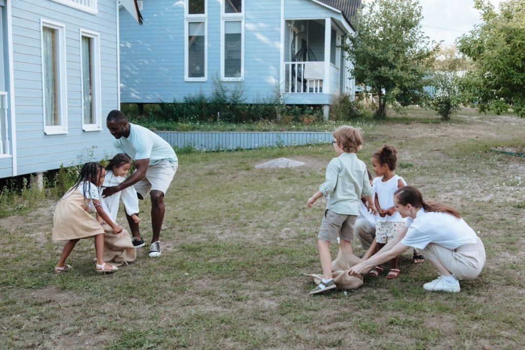 pexels-photo-10045063-10045063 Children and adults play a sack race game in a backyard, showcasing diversity and fun.