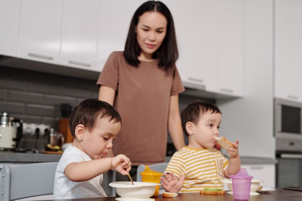 A mother watches her children enjoying breakfast in a modern kitchen setting.