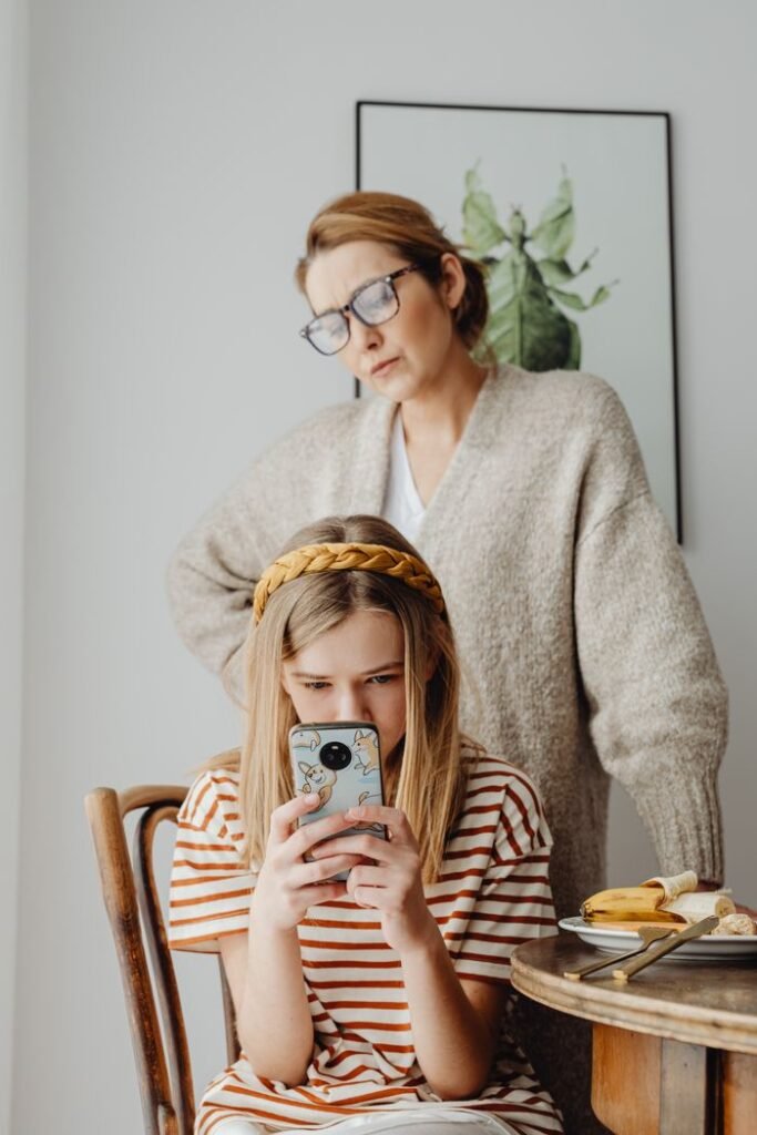 pexels-photo-6957255-6957255 A focused girl using a smartphone while her mother looks over her shoulder, indoors.
