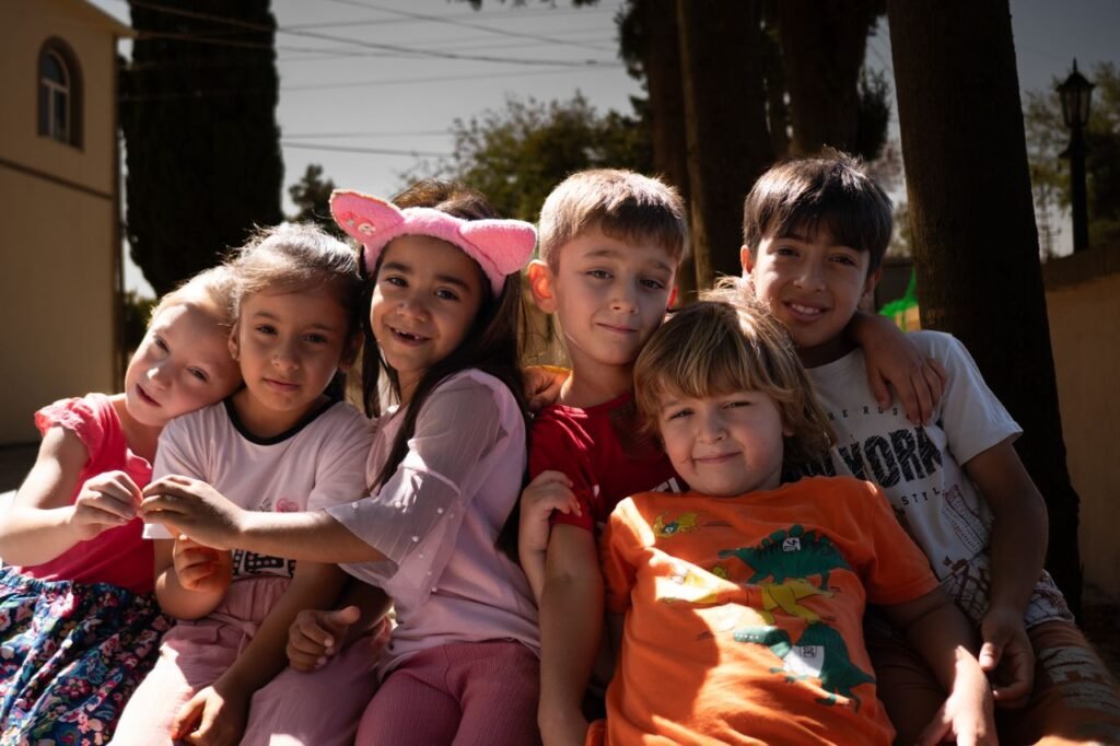 pexels-photo-33348034-33348034 A diverse group of cheerful children hugging and smiling in an outdoor setting under sunlight.