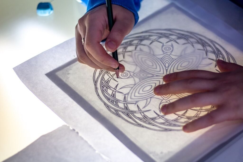pexels-photo-35075083-35075083 Close-up of hands sketching a detailed mandala on a lightbox surface.