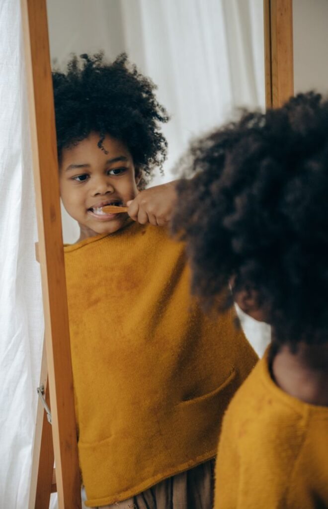 pexels-photo-4546141-4546141 From behind crop adorable content black boy with curly hair wearing orange pajama while standing against mirror and brushing teeth properly in morning