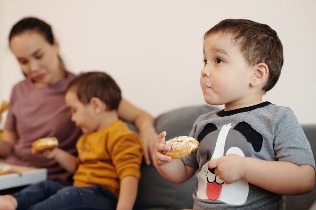 pexels-photo-6224245-6224245 A mother sitting with her two young sons enjoying donuts together indoors.