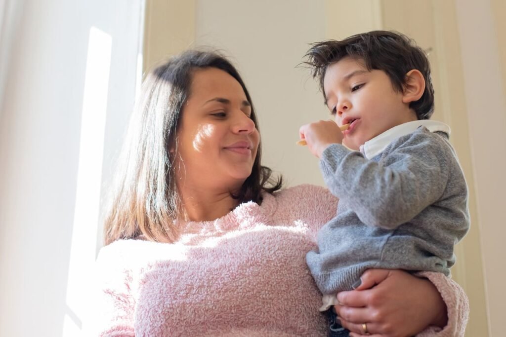 pexels-photo-7078808-7078808 Mother holding her son indoors, enjoying a snack in natural window light.