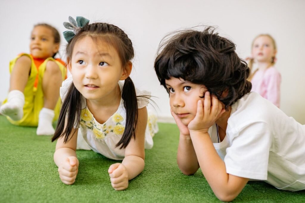 pexels-photo-8613174-8613174 Group of children lying on grass indoors, enjoying a playful learning activity in kindergarten.