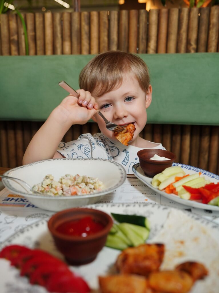 A young child happily eating a meal with fresh vegetables and dip.