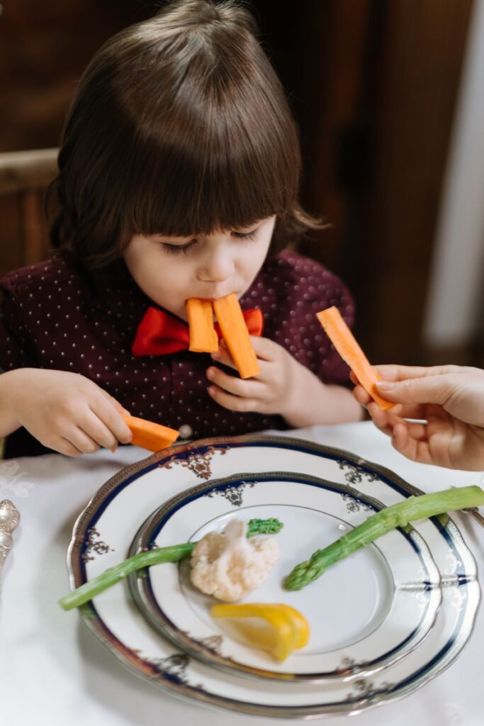 A young child playfully munching on carrot sticks at a dining table.