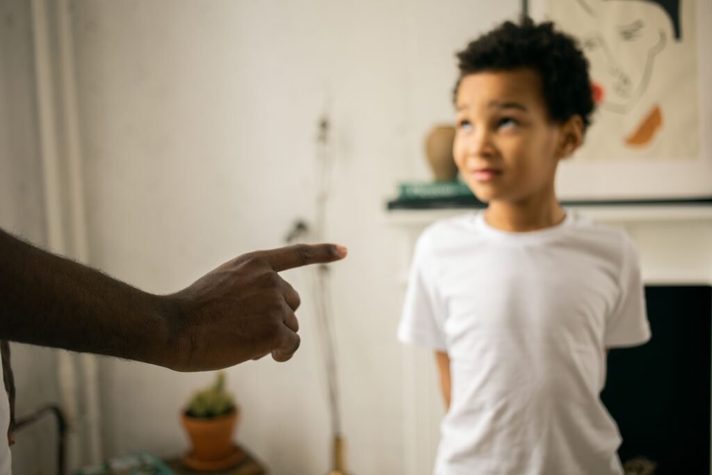 Crop unrecognizable strict black man scolding and disciplining guilty attentive little son standing with hands behind back and looking up