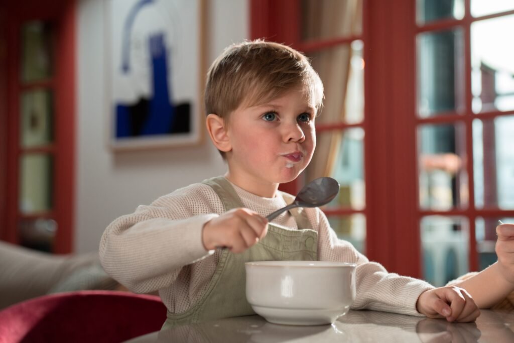 A young boy happily eating breakfast inside a cozy room, capturing a warm family moment.